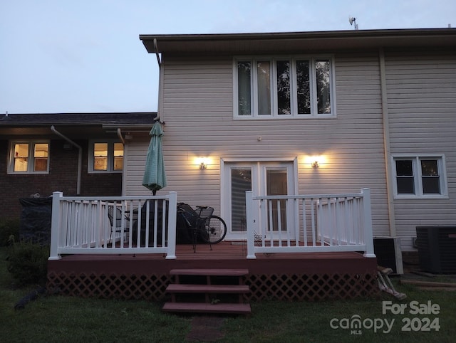 back house at dusk with central air condition unit, a wooden deck, and a lawn