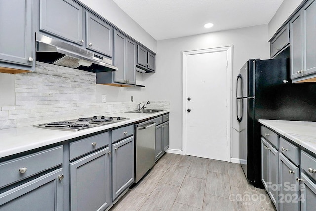 kitchen with gray cabinetry, backsplash, stainless steel appliances, sink, and light wood-type flooring