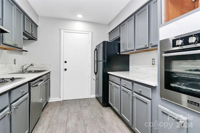 kitchen featuring stainless steel appliances, gray cabinets, backsplash, and light hardwood / wood-style floors