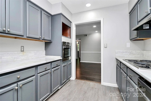 kitchen featuring range hood, appliances with stainless steel finishes, light hardwood / wood-style floors, gray cabinets, and a textured ceiling