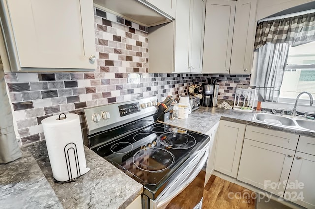 kitchen with light wood-type flooring, tasteful backsplash, sink, and electric range