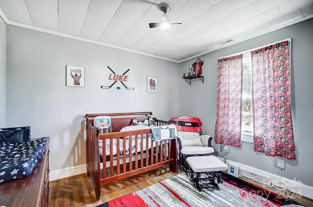 bedroom with crown molding, a crib, and wood-type flooring