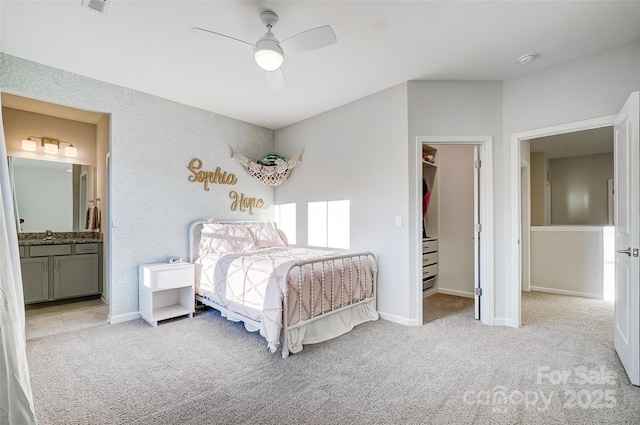 bedroom featuring a walk in closet, light carpet, connected bathroom, and ceiling fan