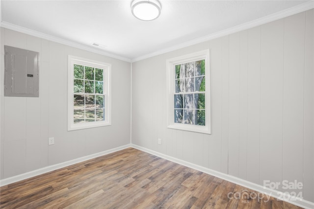 empty room featuring a wealth of natural light, electric panel, ornamental molding, and hardwood / wood-style floors