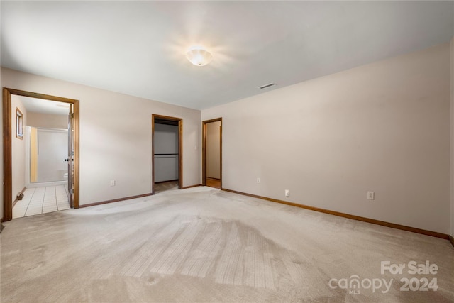 unfurnished bedroom featuring connected bathroom, a closet, and light colored carpet