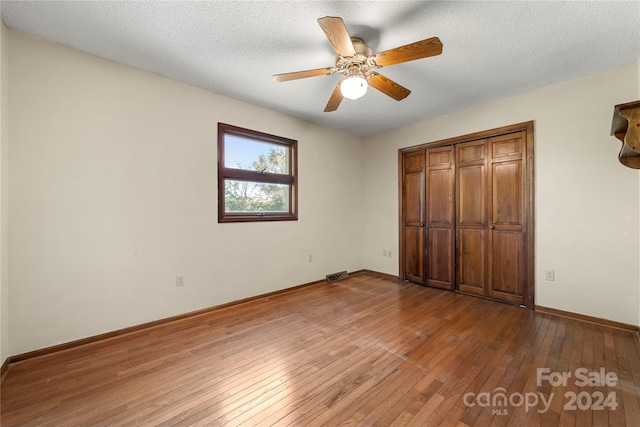 unfurnished bedroom featuring a closet, a textured ceiling, hardwood / wood-style flooring, and ceiling fan