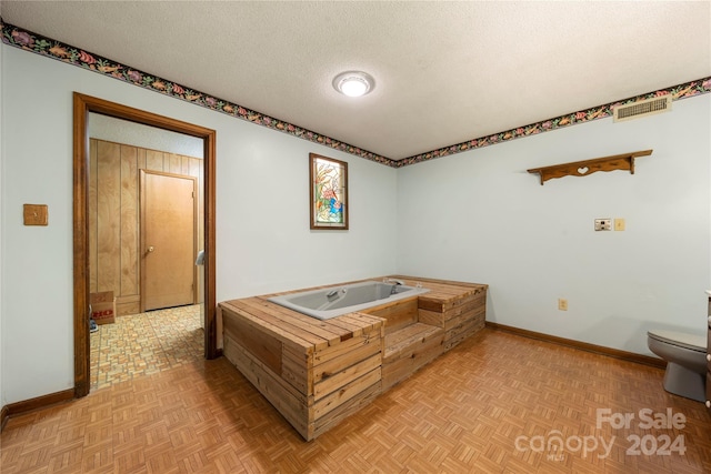 bathroom featuring a tub to relax in, parquet floors, a textured ceiling, and toilet