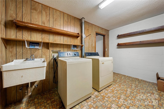 clothes washing area featuring washer and dryer, a textured ceiling, wooden walls, and sink