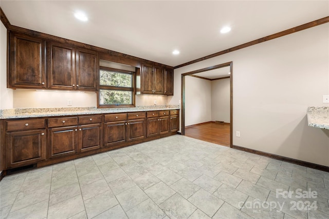 kitchen featuring dark brown cabinets, light stone counters, and ornamental molding