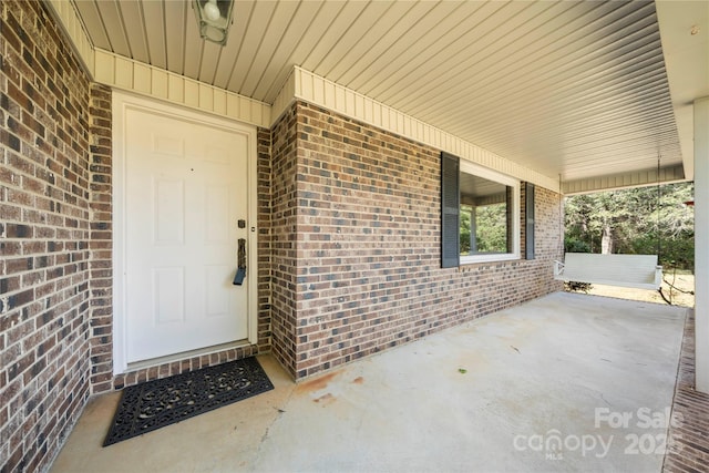 doorway to property with covered porch and brick siding