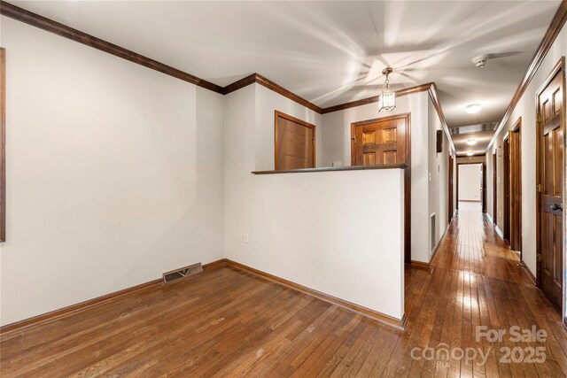 empty room with crown molding, visible vents, dark wood finished floors, and baseboards