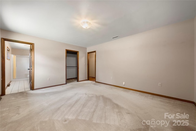 unfurnished bedroom featuring ensuite bathroom, light carpet, visible vents, baseboards, and a closet