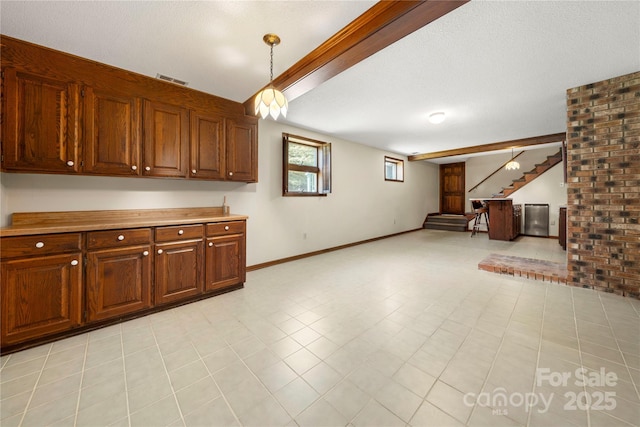 interior space with baseboards, open floor plan, beamed ceiling, decorative light fixtures, and light countertops