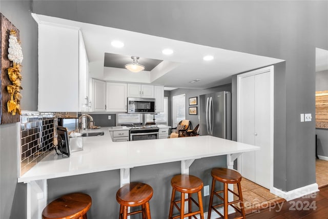 kitchen with white cabinets, light wood-type flooring, appliances with stainless steel finishes, sink, and kitchen peninsula