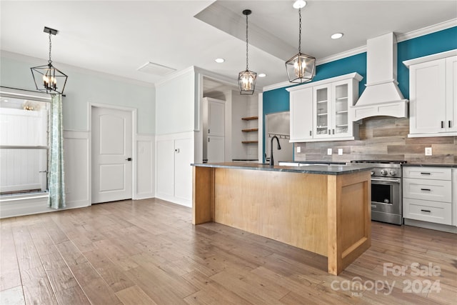 kitchen featuring white cabinetry, custom range hood, a kitchen island with sink, and stainless steel stove