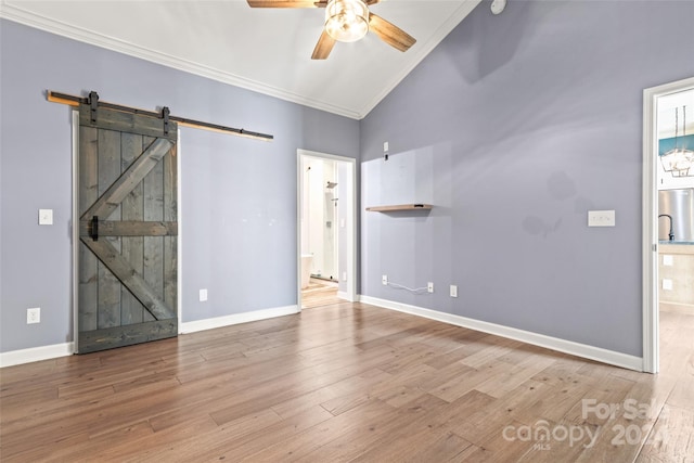 empty room featuring ceiling fan, a barn door, crown molding, and light hardwood / wood-style flooring