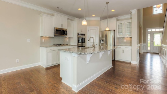 kitchen with a kitchen island with sink, tasteful backsplash, light stone counters, dark wood-type flooring, and appliances with stainless steel finishes