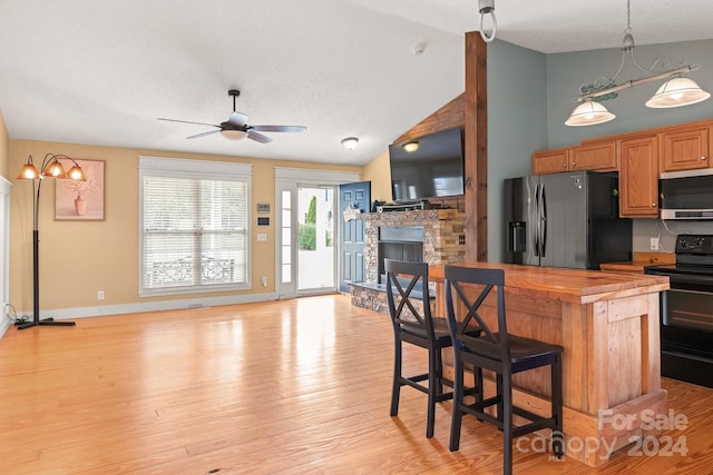 kitchen featuring light wood-type flooring, stainless steel appliances, wooden counters, ceiling fan, and a stone fireplace