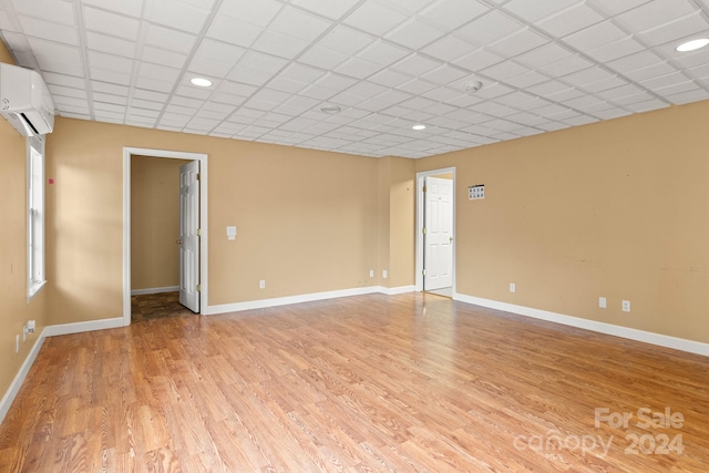 empty room featuring light wood-type flooring, a wall mounted air conditioner, and a drop ceiling