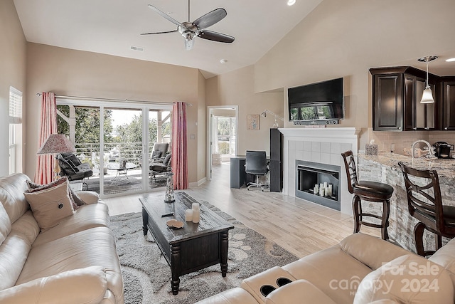 living room with a fireplace, light wood-type flooring, high vaulted ceiling, sink, and ceiling fan