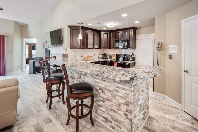 kitchen with light stone counters, light hardwood / wood-style floors, black appliances, kitchen peninsula, and a kitchen breakfast bar