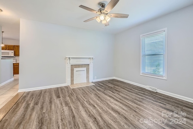 unfurnished living room with ceiling fan, a tiled fireplace, and wood-type flooring