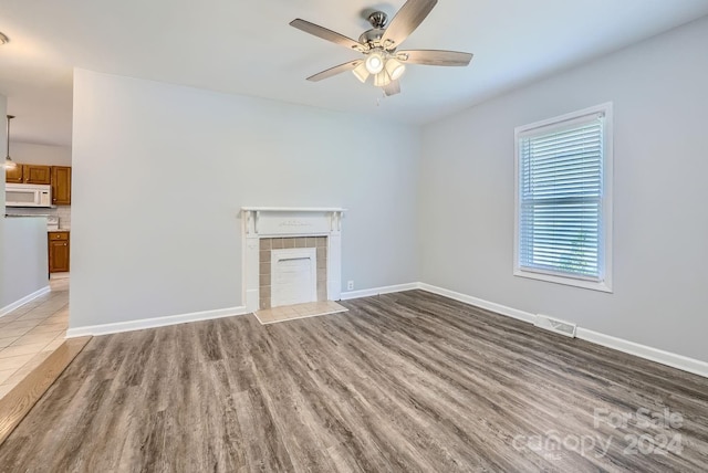 unfurnished living room with visible vents, a ceiling fan, wood finished floors, baseboards, and a tile fireplace