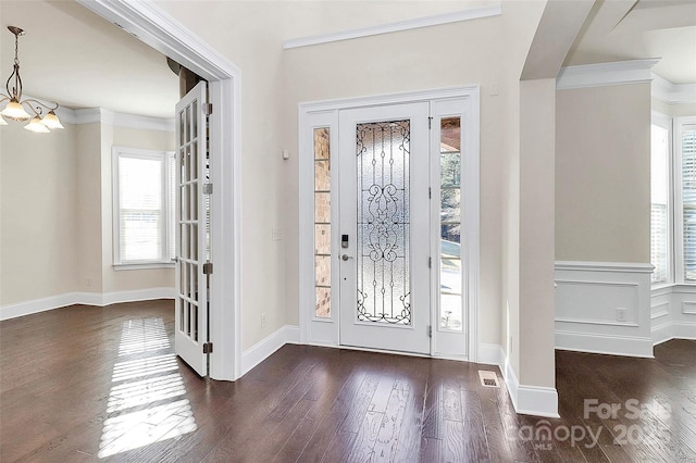 foyer entrance featuring dark hardwood / wood-style flooring, ornamental molding, and a chandelier