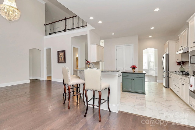 kitchen with a breakfast bar area, hanging light fixtures, stainless steel appliances, white cabinets, and kitchen peninsula