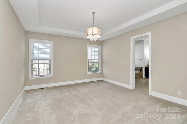 carpeted empty room with a tray ceiling and a notable chandelier