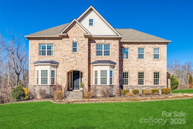 view of front of house featuring brick siding, a front yard, and a shingled roof