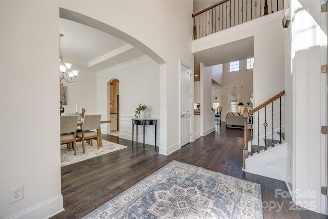 foyer featuring arched walkways, a notable chandelier, stairway, a towering ceiling, and wood finished floors