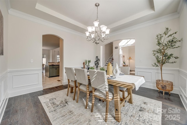 dining space featuring a notable chandelier, arched walkways, a raised ceiling, and dark wood-type flooring