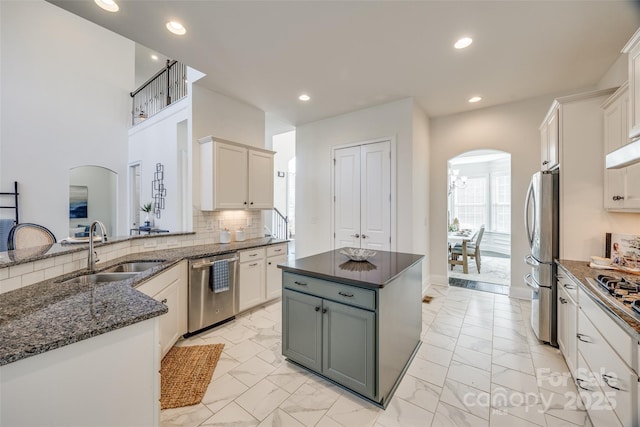 kitchen featuring appliances with stainless steel finishes, arched walkways, a sink, and decorative backsplash