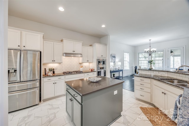 kitchen with recessed lighting, under cabinet range hood, a sink, appliances with stainless steel finishes, and decorative backsplash