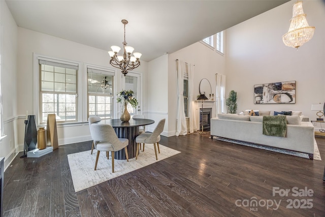 dining space featuring wood finished floors, a towering ceiling, baseboards, a glass covered fireplace, and an inviting chandelier