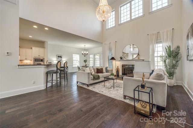 living room with dark wood-type flooring, a glass covered fireplace, and an inviting chandelier