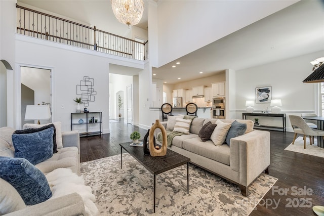 living area with arched walkways, a chandelier, recessed lighting, baseboards, and dark wood-style floors