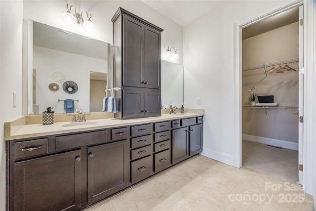 bathroom with double vanity, a spacious closet, baseboards, and a sink