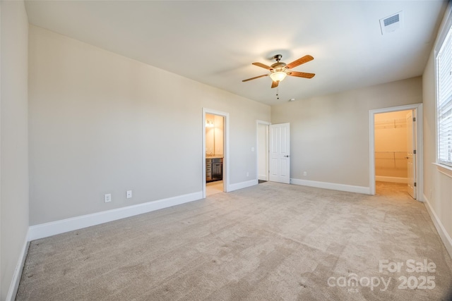 unfurnished bedroom with connected bathroom, light colored carpet, visible vents, baseboards, and a walk in closet