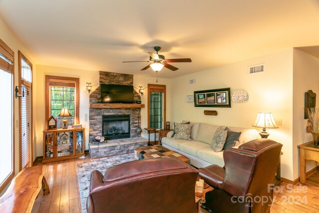 living room with light hardwood / wood-style flooring, ceiling fan, and a stone fireplace