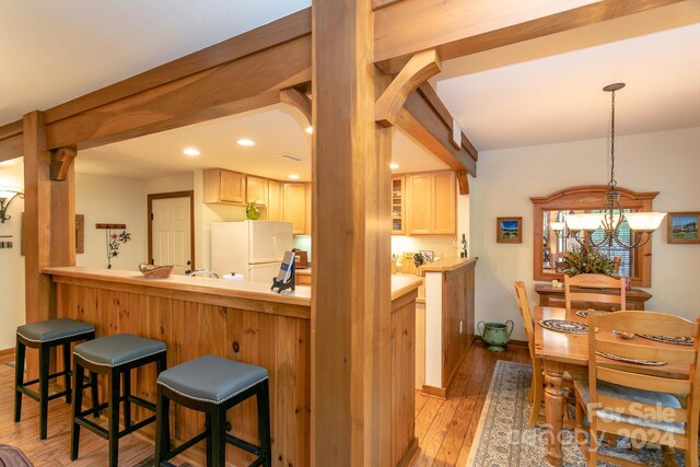 kitchen featuring white fridge, light hardwood / wood-style flooring, a notable chandelier, a breakfast bar, and light brown cabinets