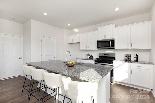 kitchen with an island with sink, dark wood-type flooring, white cabinetry, stainless steel appliances, and light stone countertops