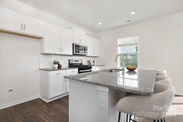 kitchen with stainless steel appliances, stone counters, a kitchen island with sink, and sink