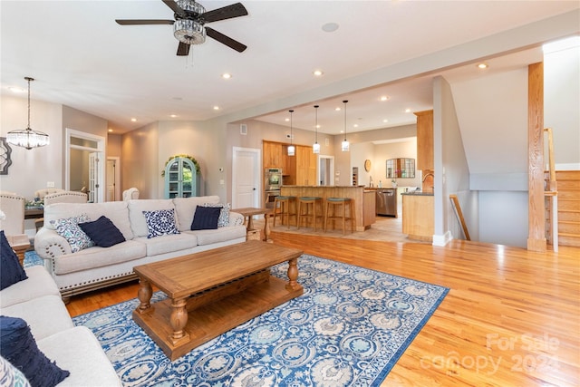 living room with light wood-type flooring and ceiling fan with notable chandelier