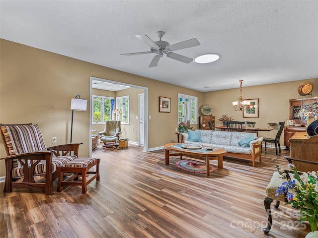 living room with hardwood / wood-style flooring, ceiling fan with notable chandelier, and a textured ceiling