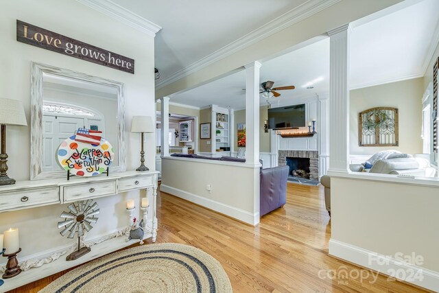 hall with light wood-type flooring, crown molding, and ornate columns