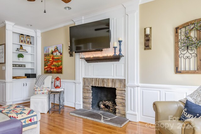 living room featuring light wood-type flooring, crown molding, ceiling fan, and a stone fireplace