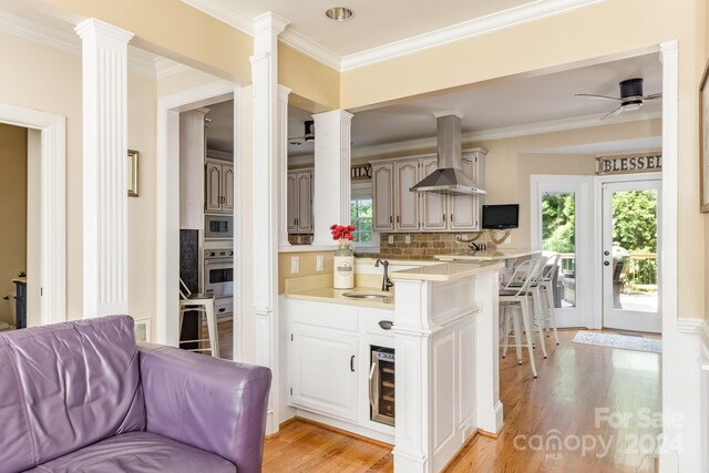 kitchen with appliances with stainless steel finishes, ornate columns, ceiling fan, and wall chimney range hood