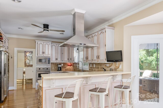 kitchen featuring appliances with stainless steel finishes, a breakfast bar area, island exhaust hood, kitchen peninsula, and ceiling fan